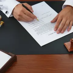 Podpisanie dokumentu dotyczącego przepisania mieszkania na dziecko. Na biurku znajdują się pieczęcie i dokumenty.