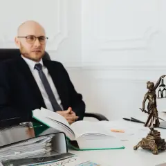 Prawnik w garniturze siedzi przy biurku, obok niego stos dokumentów i otwarta księga. Zastanawiasz się, ile kosztuje notariusz?