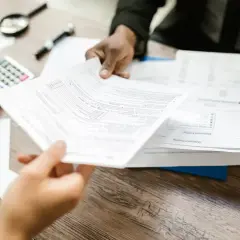 Przekazywanie dokumentów, w tym deklaracji podatku od nieruchomości, na drewnianym biurku.