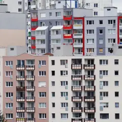 Wielopiętrowe bloki mieszkalne z balkonami. W jednym z mieszkań widoczna jest kartka z napisem "reklamacja z tytułu rękojmi".