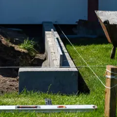Budowa fundamentu pod ogrodzenie. Betonowe bloczki i poziomica wskazują precyzyjne wykonanie.