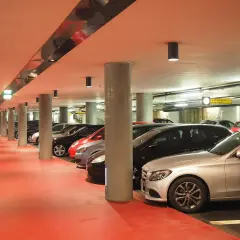 Rząd samochodów na czerwonym tle, w podziemnym miejscu postojowym.