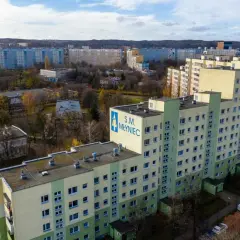 Osiedle z wielkiej płyty S.M. Młyniec, z charakterystycznymi blokami mieszkalnymi w pastelowych kolorach, otoczone jesienną zielenią i drzewami.