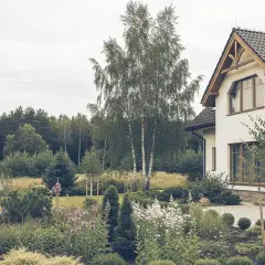 Piękny dom bliźniak z ogrodem pełnym kwiatów i drzew, otoczony lasem.