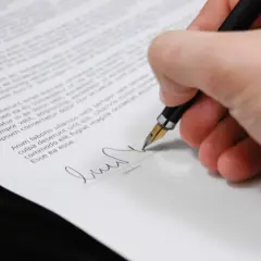 Podpisanie umowy przedwstępnej sprzedaży działki. Długopis z piórem kreśli podpis na dokumencie.