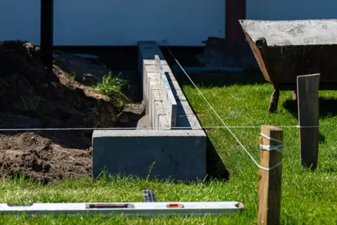 Budowa fundamentu pod ogrodzenie. Betonowe bloczki i poziomica wskazują precyzyjne wykonanie.