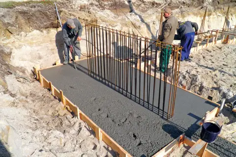 Budowa fundamentów: pracownicy wylewają beton na zbrojenie, tworząc solidny żelbeton.