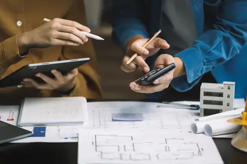 Architekci analizują plany, liczą koszty i omawiają, ile kosztuje odbiór domu. Na stole szkice, tablet, kalkulator i model budynku.