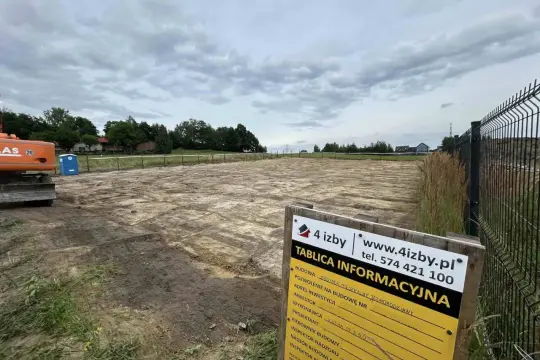 Tablica informacyjna budowy z danymi wykonawcy i inwestora na tle placu budowy.