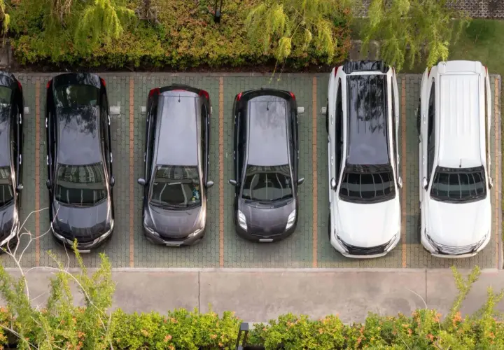 Widok z góry na rząd samochodów na parkingu. Widać odległość miejsc postojowych od granicy działki, otoczonej zielenią.