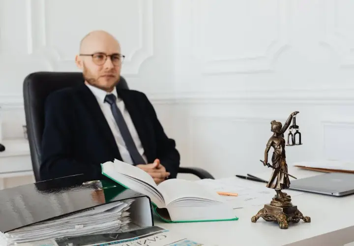 Prawnik w garniturze siedzi przy biurku, obok niego stos dokumentów i otwarta księga. Zastanawiasz się, ile kosztuje notariusz?