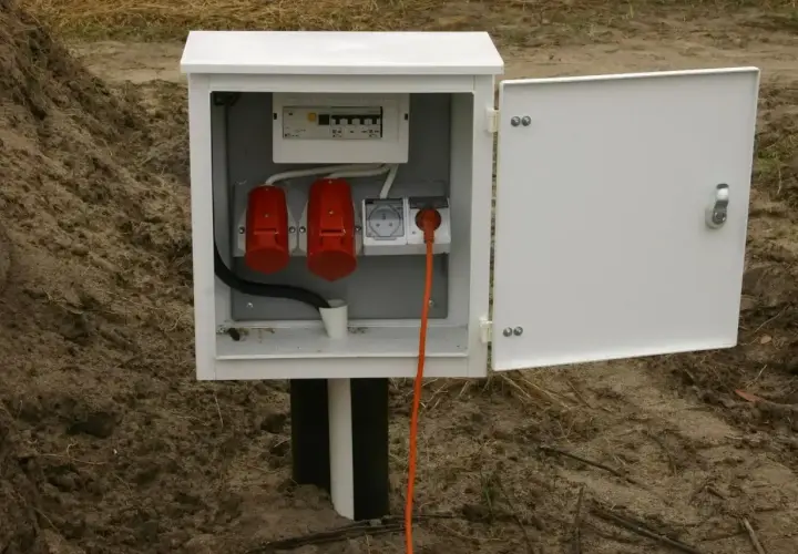 Skrzynka elektryczna na działce bez domu, gotowa do podłączenia prądu. Widoczne gniazda i zabezpieczenia.