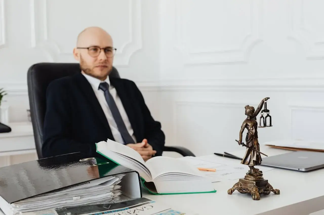Prawnik w garniturze siedzi przy biurku, obok niego stos dokumentów i otwarta księga. Zastanawiasz się, ile kosztuje notariusz?
