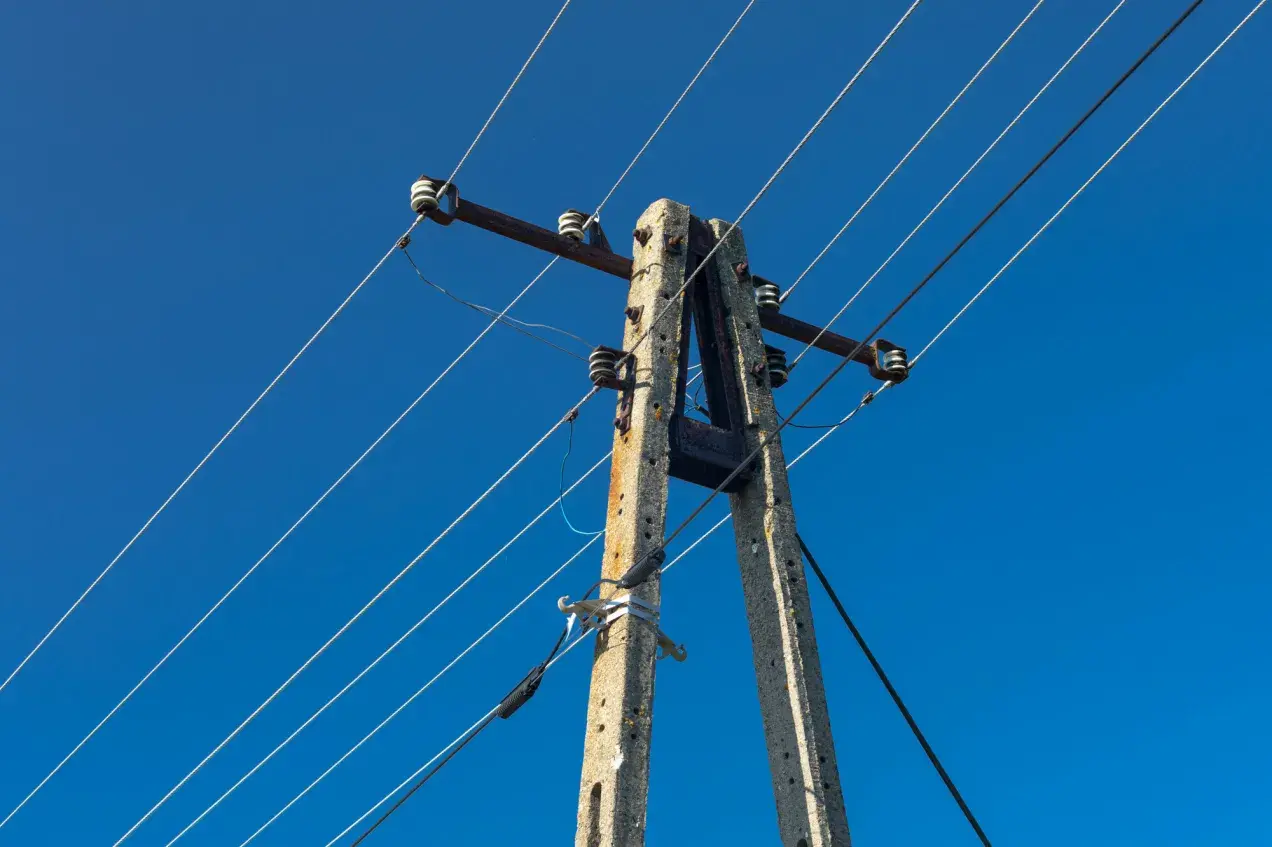 Betonowy słup energetyczny z przewodami pod błękitnym niebem. Zastanawiasz się, ile wynosi odszkodowanie za słupy energetyczne na działce?