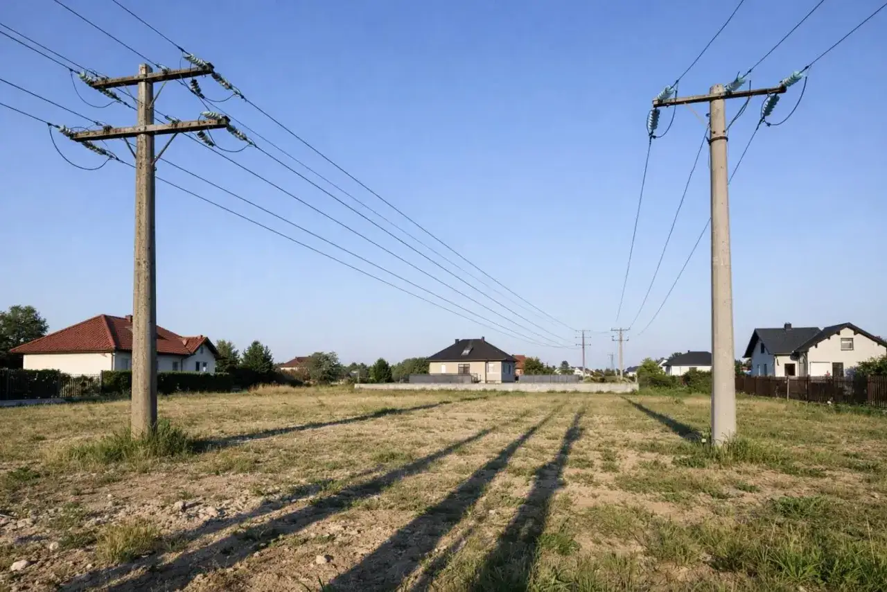 Słupy energetyczne na działce. Zastanawiasz się, ile wynosi odszkodowanie za słupy energetyczne na działce? W tle domy jednorodzinne.