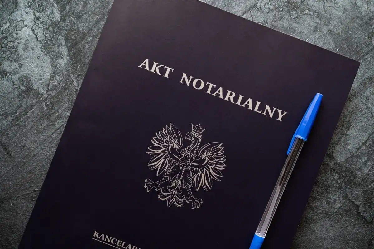 Akt notarialny z godłem Polski i długopisem, gotowy do sfinalizowania przeniesienia własności nieruchomości.