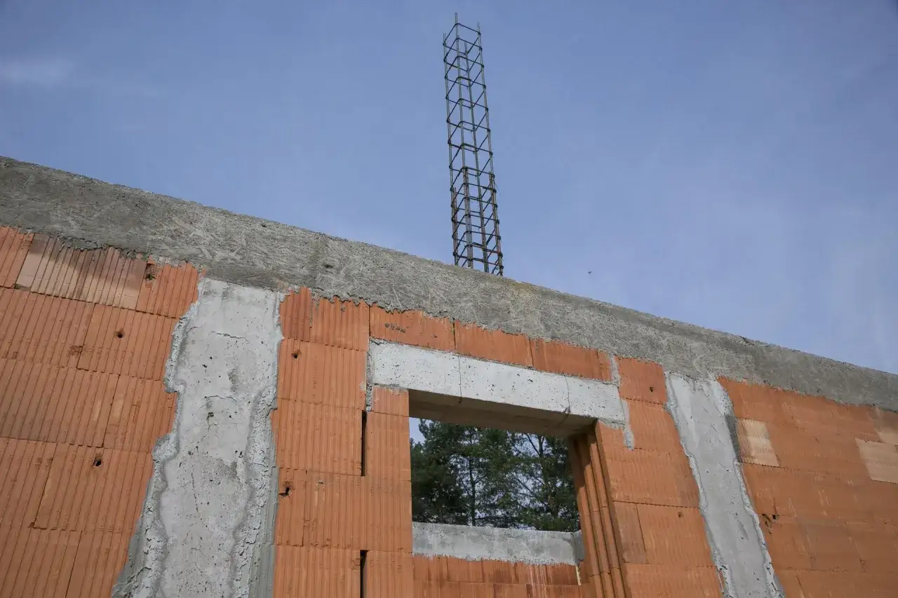 Wieniec budowlany zbrojony, betonowy, na ścianie z pustaków ceramicznych, z widocznym szalunkiem i prętami zbrojeniowymi.