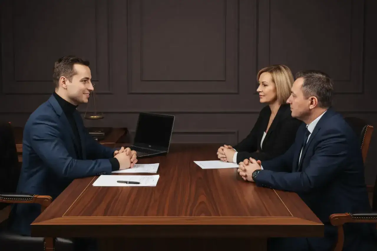 Trzy osoby przy drewnianym stole omawiają sprzedaż mieszkania przed upływem 5 lat.