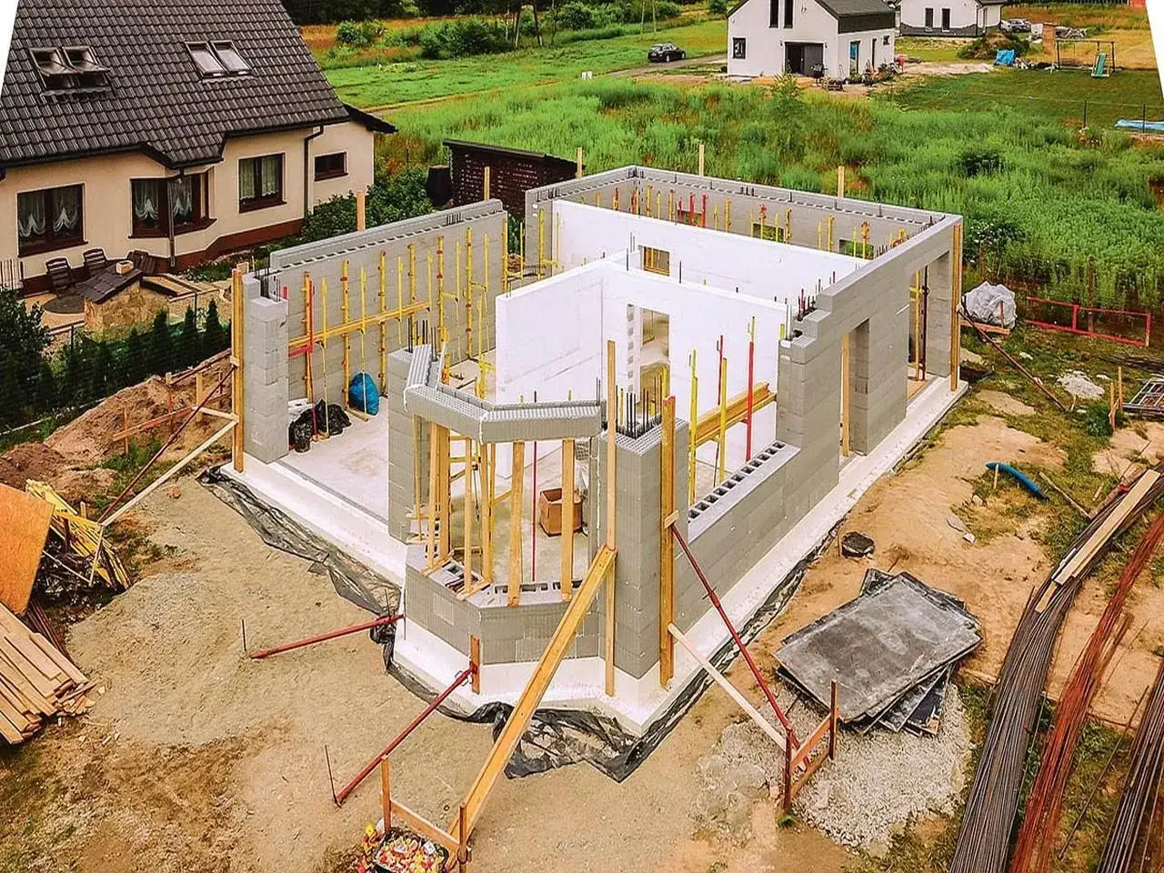 Budowa domu ze styropianu w toku. Ściany z bloczków, zbrojenie i drewniane podpory tworzą zarys przyszłego domu.