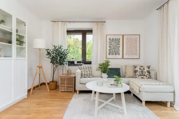 Przytulny salon, idealne **mieszkanie dla młodych**. Jasna sofa, stolik kawowy, rośliny i botaniczne plakaty tworzą relaksującą atmosferę.